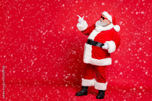 Full length profile side photo of charming santa claus in eyewear eyeglasses showing promo wearing bright costume belt isolated over red background