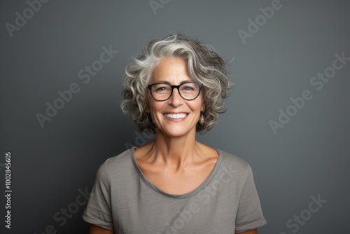 Portrait of a happy woman in her 50s dressed in a casual t-shirt while standing against plain cyclorama studio wall