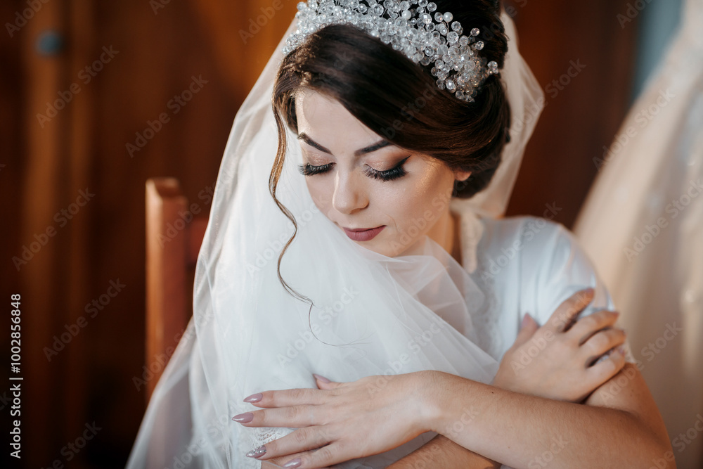 Fototapeta premium A woman wearing a white dress and a tiara. She is sitting on a chair. The chair is wooden