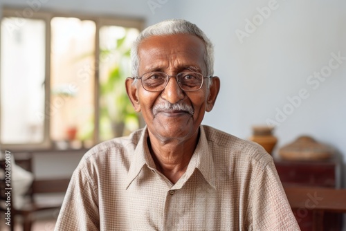 Portrait of a tender indian man in his 80s wearing a comfy flannel shirt in crisp minimalistic living room