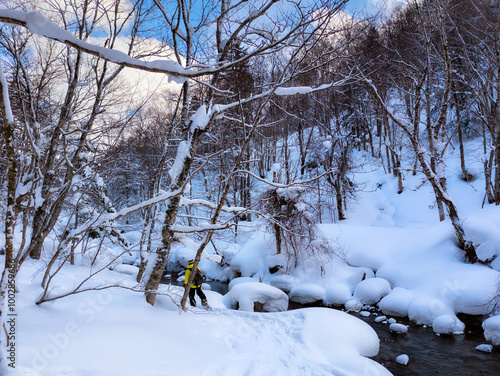 Female hiker next to a small river in a snow covered forest photo