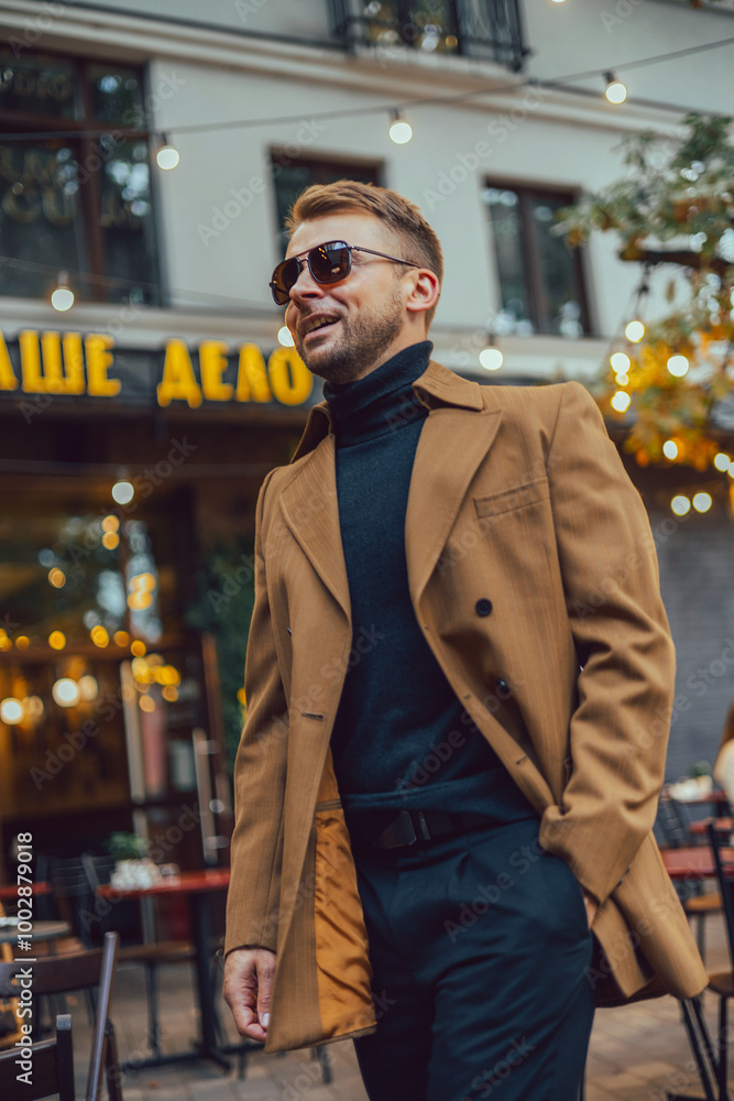 Fototapeta premium young guy with a beard and mustache with glasses in a suit posing on the street in the sunlight, fashion man, style, vintage style, retro men, handsome beard, outdoor portrait, close up