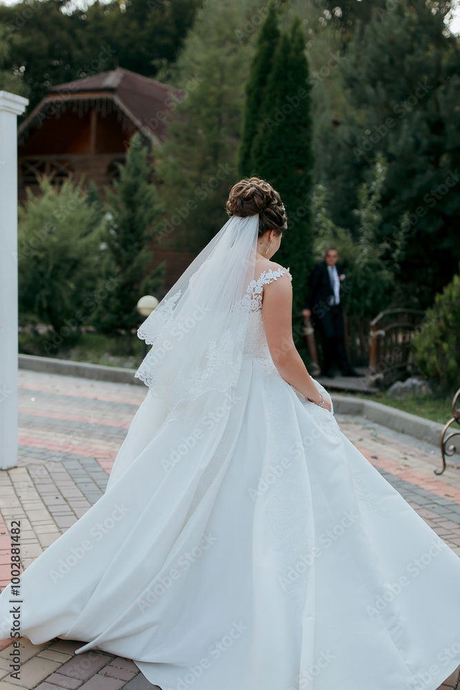 Obraz premium A woman in a white wedding dress is walking down a brick walkway. A man is standing behind her