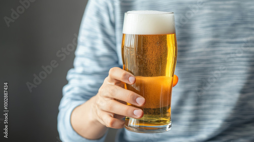 A person holding a glass of beer in their hand, the light reflecting off the foam and the amber liquid The image conveys a casual and relaxed moment photo