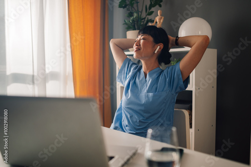 Photography Relaxed asian woman nurse in blue scrubs stretching while sitting at desk