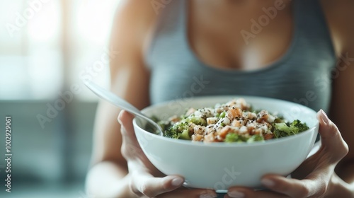 A bowl filled with nutritious broccoli and grains is held in strong hands, depicting a commitment to healthy lifestyle and nourishment amidst a bright kitchen setting.