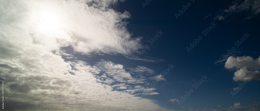 Obraz premium Sun shining through the puffy clouds. White clouds banner. Beautiful clouds. Background with clouds on blue sky. Summer Cloud on blue sky.