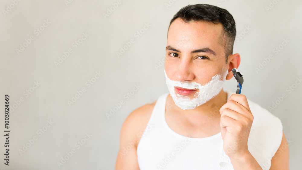 Young man is starting his morning routine by applying shaving cream to his face Young man is starting his morning routine by applying shaving cream to his face