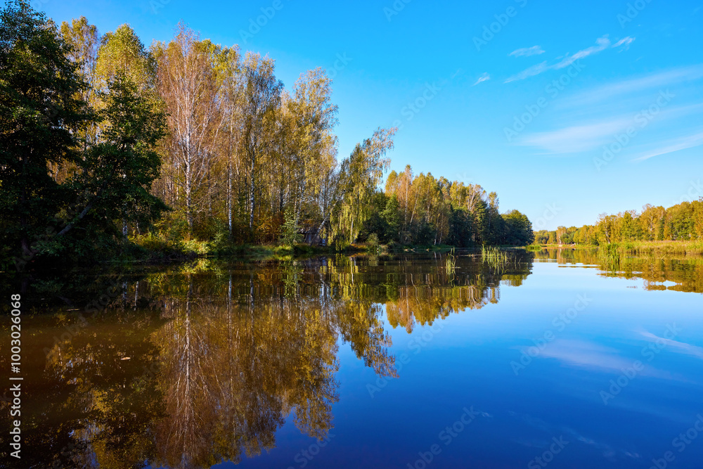 A serene river mirrors the golden hues of trees on a clear autumn day, showcasing nature’s symmetry A serene river mirrors the golden hues of trees on a clear autumn day, showcasing nature’s symmetry