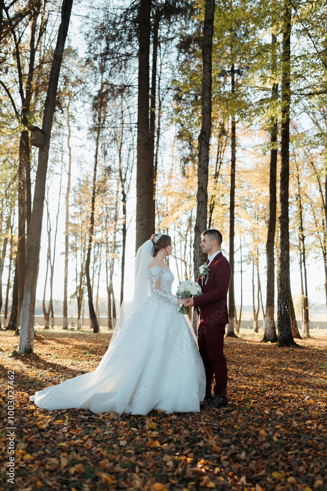 A bride and groom stand in a forest, surrounded by trees and leaves. The bride is wearing a white dress and the groom is wearing a red suit. They are holding hands and smiling, looking happy A bride and groom stand in a forest, surrounded by trees and leaves. The bride is wearing a white dress and the groom is wearing a red suit. They are holding hands and smiling, looking happy