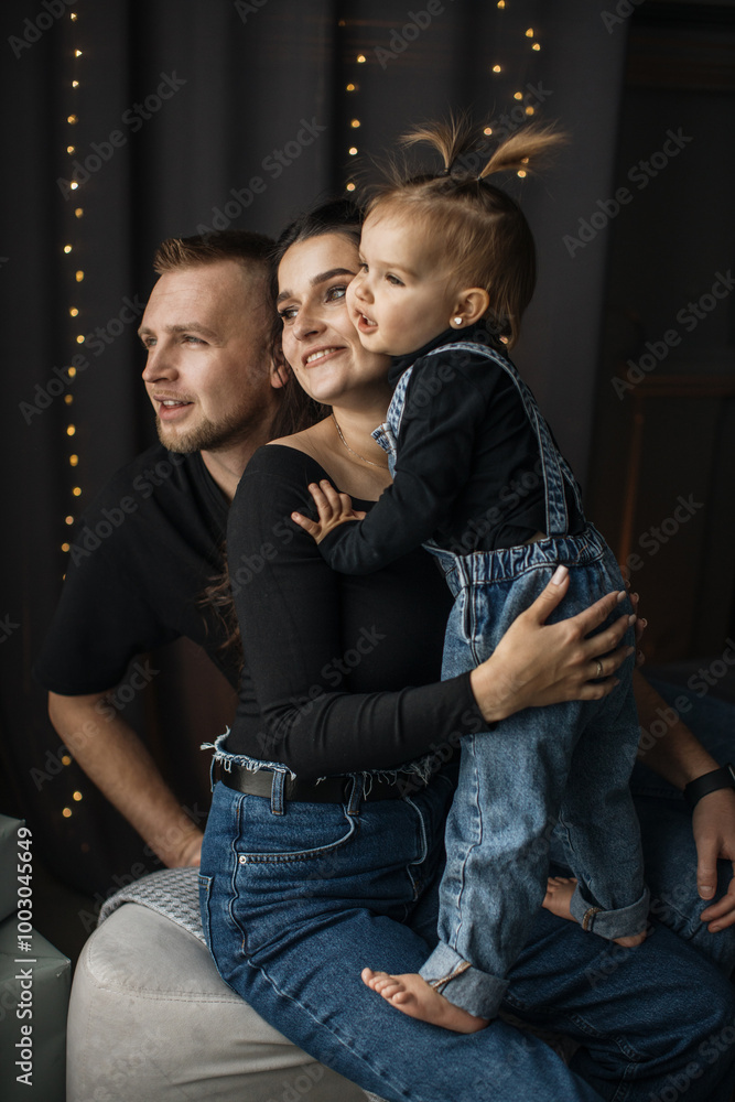 Obraz premium Young Caucasian father and mother with toddler indoors. Family enjoying quality time together with smiles and warm atmosphere. Baby wearing denim outfit, parents in casual attire.