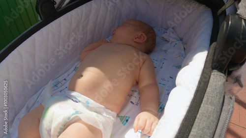 An infant is lying in a pram cradle with one nappy on. Close-up view. A walk with the baby in the fresh air