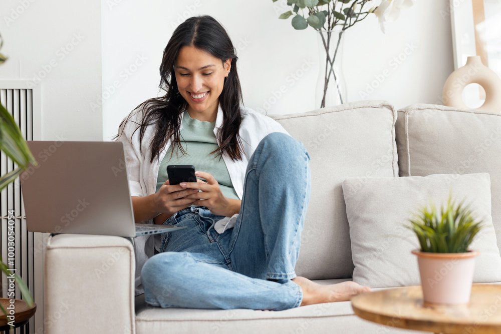 Beautiful woman working with her laptop while using mobile phone sitting on a couch at home Beautiful woman working with her laptop while using mobile phone sitting on a couch at home