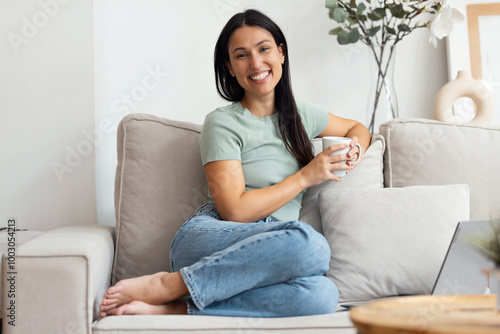 Free Download Pretty young woman working with her laptop while drinking a cup of coffee sitting on a couch at home - GFXLoad