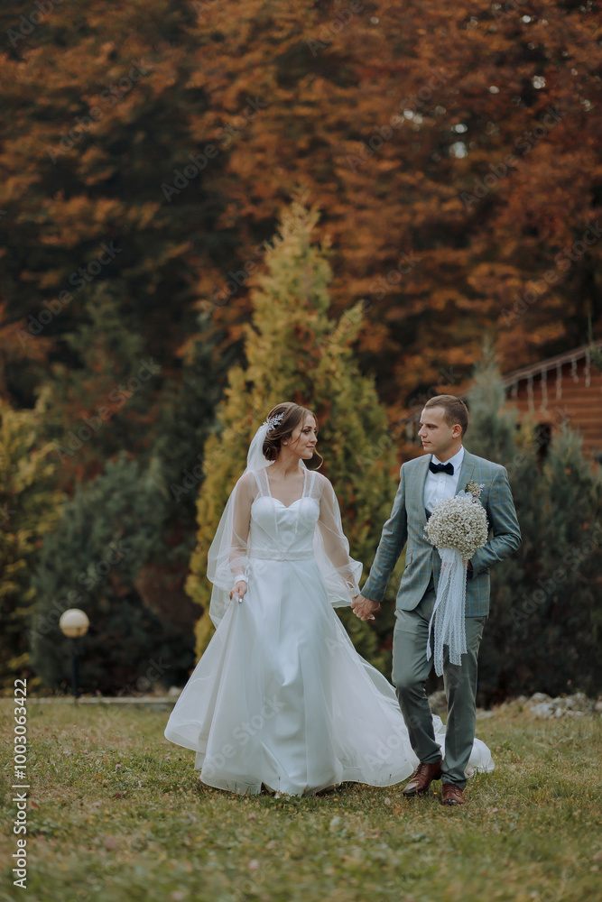 A bride and groom are walking together in a field. The bride is wearing a white dress and the groom is wearing a suit. They are holding hands and smiling A bride and groom are walking together in a field. The bride is wearing a white dress and the groom is wearing a suit. They are holding hands and smiling