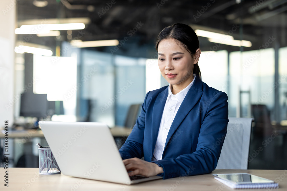 Asian businesswoman concentrating on laptop in modern office setting. Displays professionalism, focus, and confidence in business environment, ideal for concepts of technology, career Asian businesswoman concentrating on laptop in modern office setting. Displays professionalism, focus, and confidence in business environment, ideal for concepts of technology, career