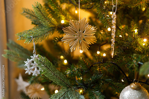Stylish christmas ornaments on tree close up. Beautiful decorated christmas tree with straw snowflake, vintage baubles and golden lights. Winter holidays preparation. Atmospheric magical eve