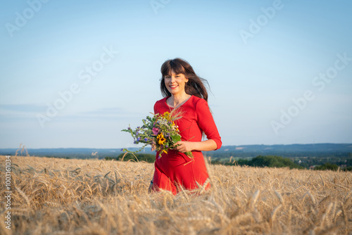 Junge und attraktive Frau mit einem roten Kleid in einem reifen Getreidefeld genießt den Sommer. photo