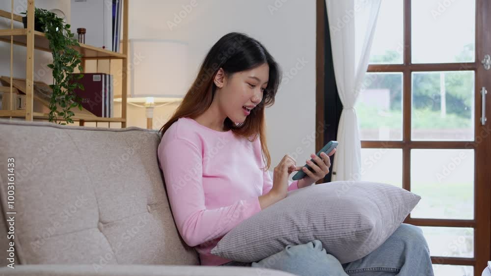 Young woman sitting on a couch, scrolling through her smartphone and receiving exciting good news, radiating happiness Young woman sitting on a couch, scrolling through her smartphone and receiving exciting good news, radiating happiness