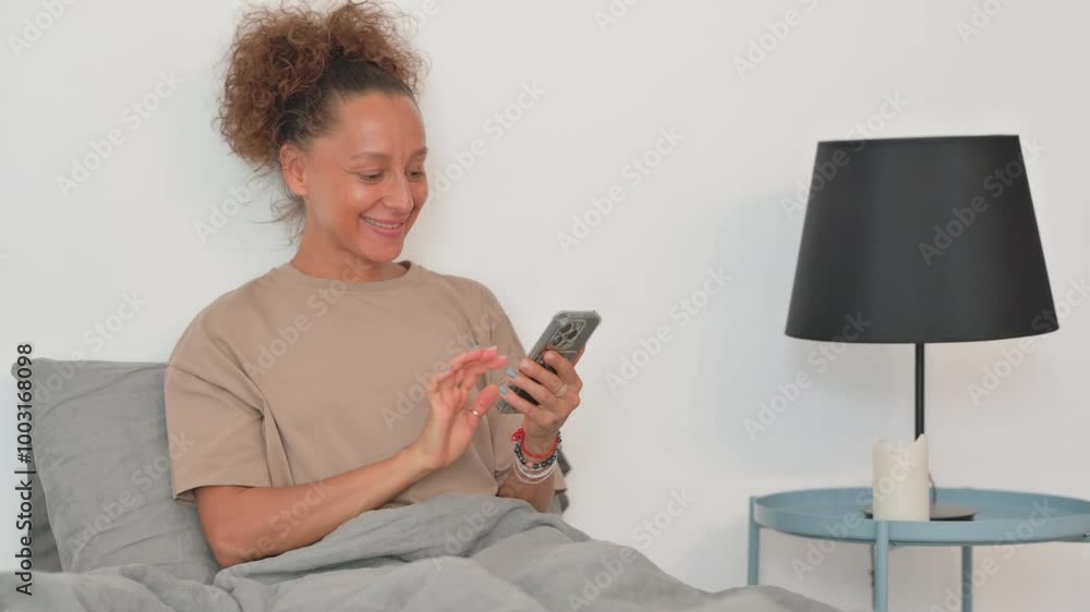 Hispanic Woman Celebrating Success on Phone while Sitting in Bed Hispanic Woman Celebrating Success on Phone while Sitting in Bed