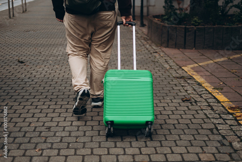 Obraz na płótnie Unrecognizable man pulling green suitcase outdoors. Rear view. Copy space. Man walking on the street with travel bag. w salonie