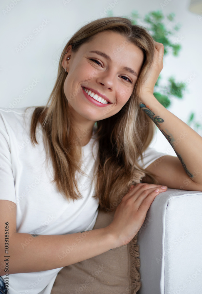 Attractive young woman lounges comfortably on white sofa, smiling and relaxing in a casual setting. She wears a white t-shirt and jeans, with soft pillows in the background, evoking comfort and ease Attractive young woman lounges comfortably on white sofa, smiling and relaxing in a casual setting. She wears a white t-shirt and jeans, with soft pillows in the background, evoking comfort and ease