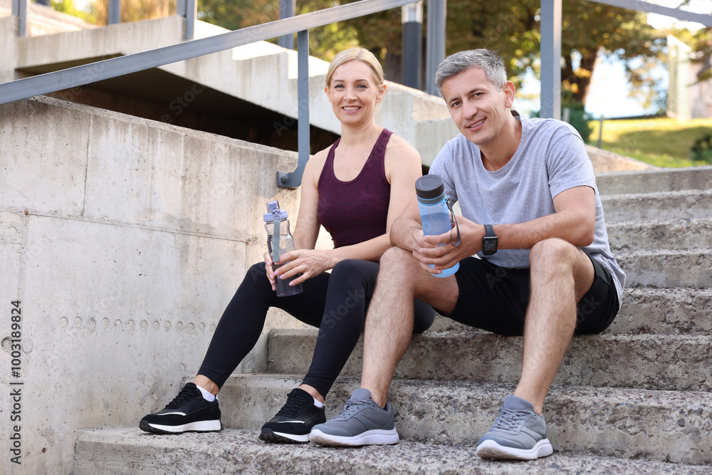 Smiling couple with bottles of water on steps outdoors Smiling couple with bottles of water on steps outdoors