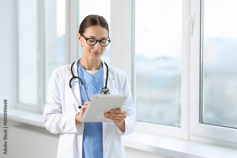 Nurse with stethoscope using tablet near window in clinic Nurse with stethoscope using tablet near window in clinic