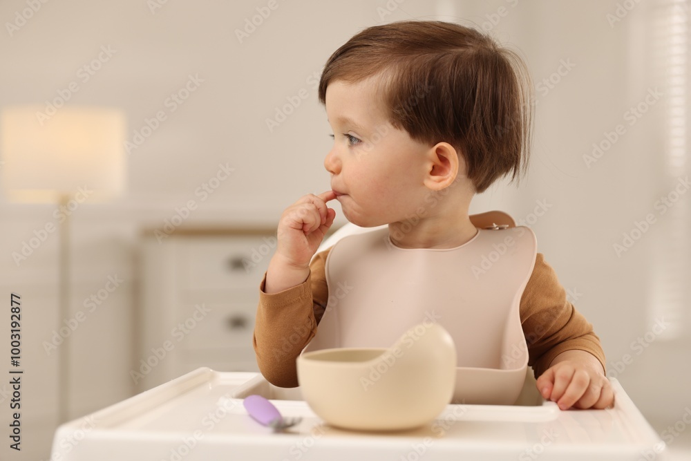 Cute little baby eating healthy food from bowl in high chair at home Cute little baby eating healthy food from bowl in high chair at home