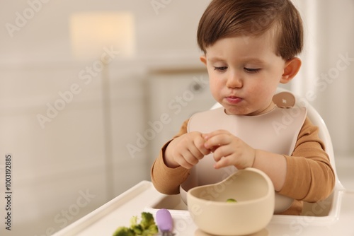 Cute little baby eating healthy food from bowl in high chair at home, space for text