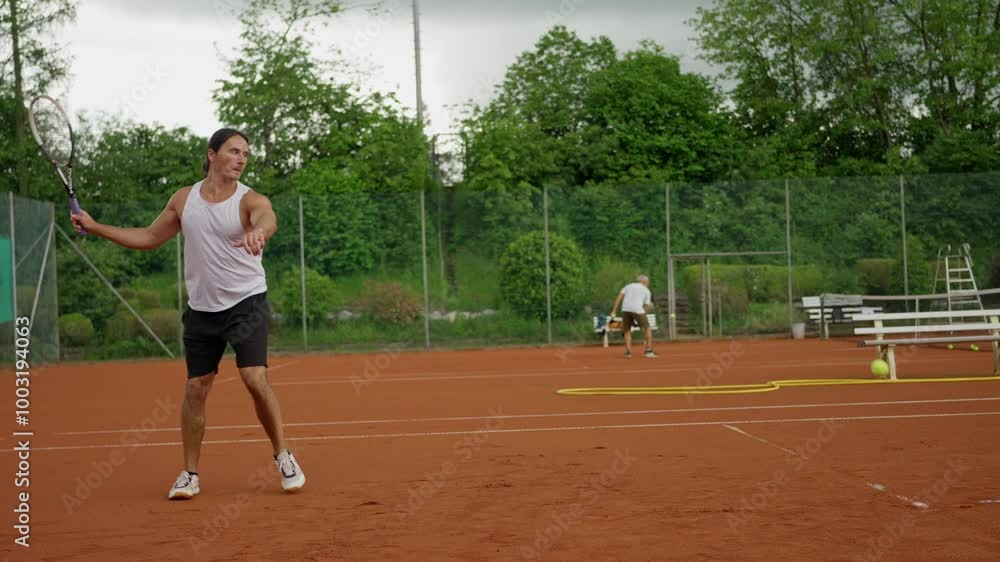 Man is playing tennis on a clay court, displaying his focus on the game Man is playing tennis on a clay court, displaying his focus on the game