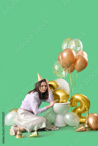 Young woman with hangover sitting near toilet bowl after Birthday party on gr...