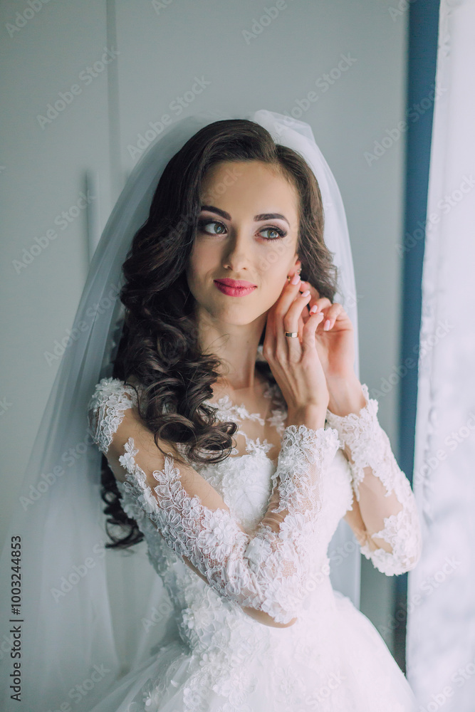 A woman in a wedding dress is looking at the camera. She is wearing a veil and has her hands on her ears A woman in a wedding dress is looking at the camera. She is wearing a veil and has her hands on her ears