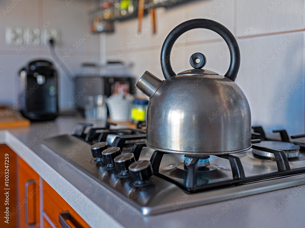 A metal kettle standing on a stove with a lit fire. A metal kettle standing on a stove with a lit fire.