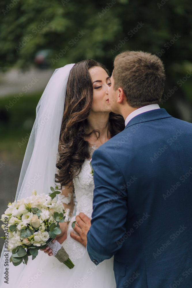 A bride and groom kiss in front of a white veil. The bride is holding a bouquet of flowers A bride and groom kiss in front of a white veil. The bride is holding a bouquet of flowers
