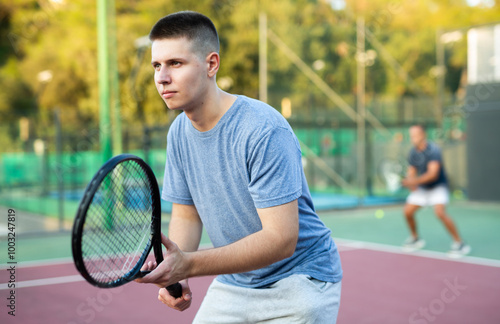 Portrait of sporty man standing with tennis racquet in his hands ready to play match in open court on summer day photo