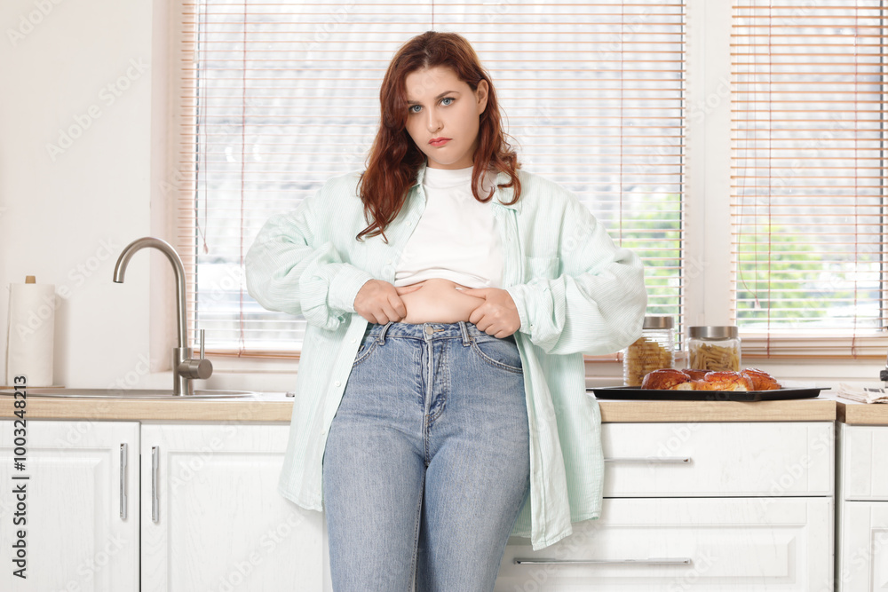 Overweight young sad woman in tight jeans touching her fat belly at home. Weight gain concept Overweight young sad woman in tight jeans touching her fat belly at home. Weight gain concept