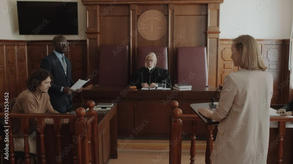 Black male attorney asking Caucasian female witness questions about suspect sitting near him during trial in courtroom, judge listening Black male attorney asking Caucasian female witness questions about suspect sitting near him during trial in courtroom, judge listening