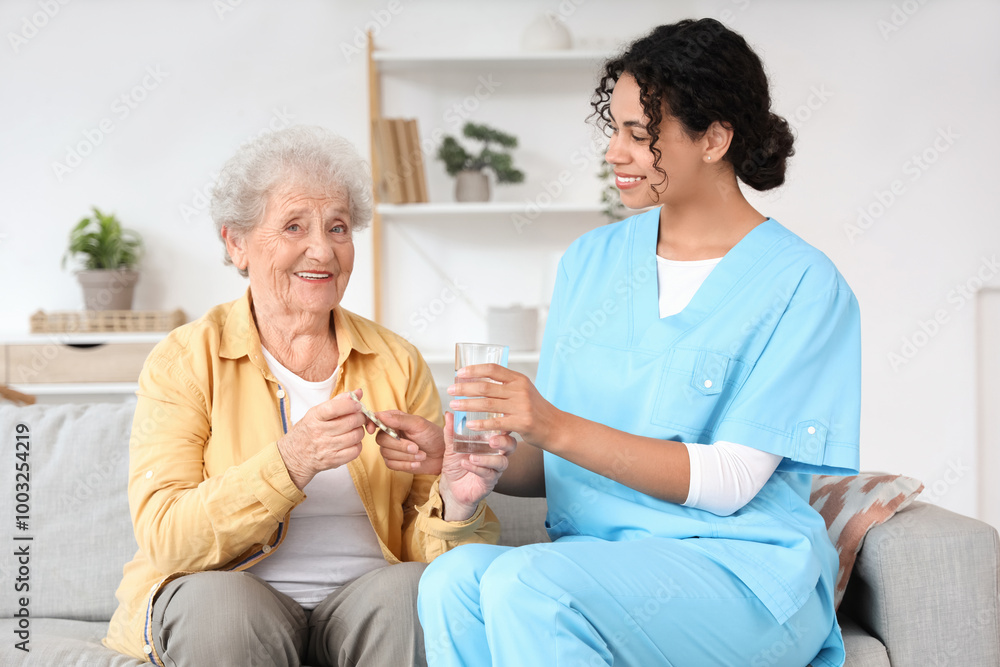 Young African-American female medical worker giving elderly woman pills and glass of water in nursing home Young African-American female medical worker giving elderly woman pills and glass of water in nursing home