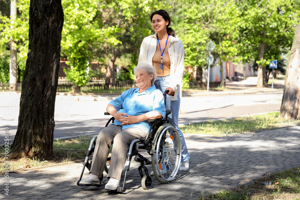 Young African-American female medical worker walking with elderly woman on wheelchair outdoors Young African-American female medical worker walking with elderly woman on wheelchair outdoors