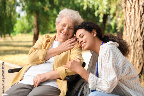 Young African-American female medical worker with elderly woman on wheelchair outdoors, closeup photo