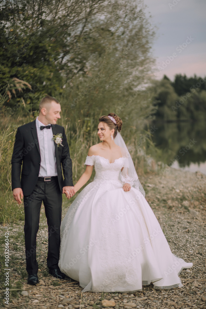 A bride and groom are walking together on a beach. The bride is wearing a white dress and the groom is wearing a suit. The couple is holding hands and smiling, creating a happy and romantic atmosphere A bride and groom are walking together on a beach. The bride is wearing a white dress and the groom is wearing a suit. The couple is holding hands and smiling, creating a happy and romantic atmosphere