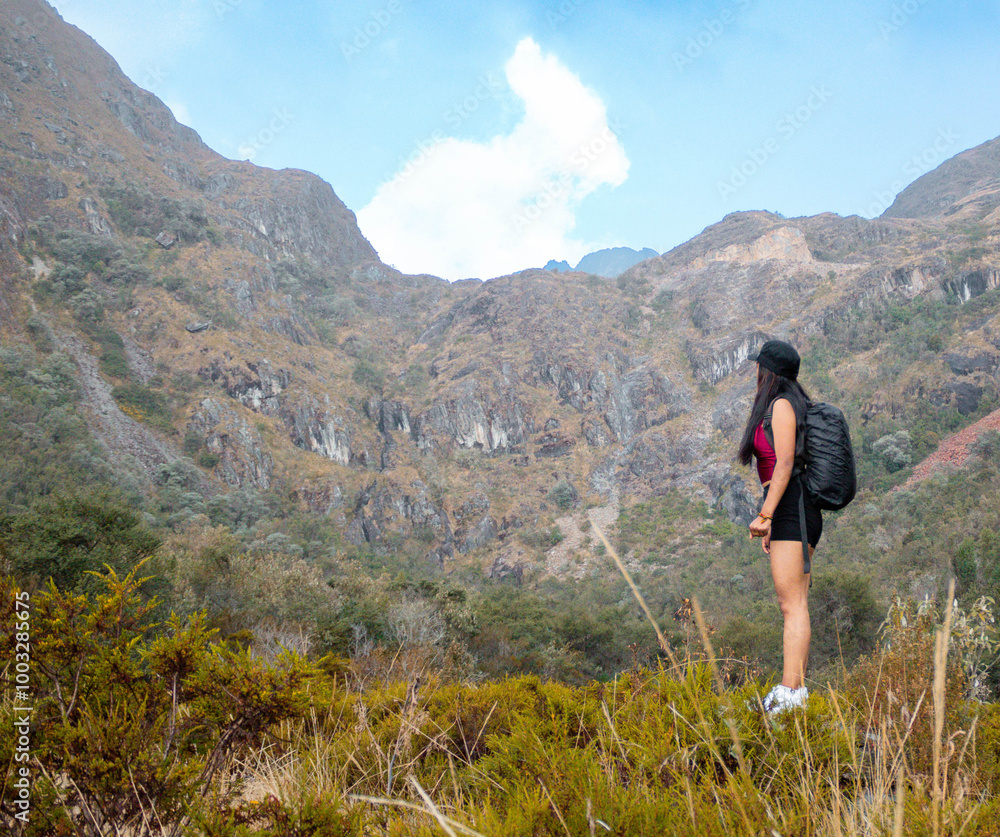 Naklejka premium Hermosas montañas y mujer joven con short y mochila en el camino concepto de turismo. Paisaje con chica deportiva con top en la cima de la montaña, bosque, colinas, cielo blancos con nubes, Viaje,