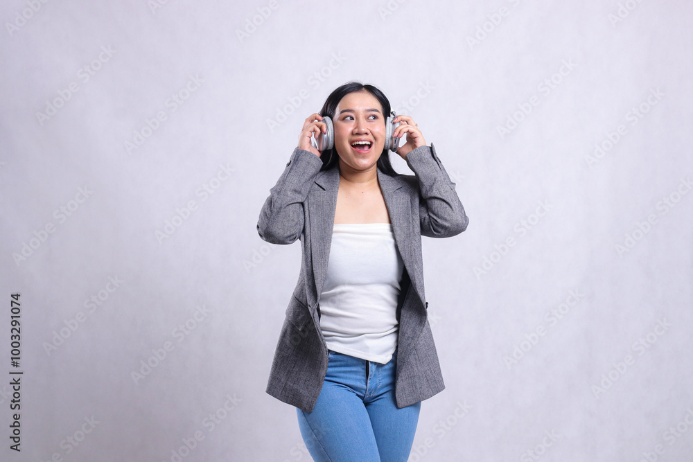 beautiful young office female asia happy candid holding and wearing headphone headset listening music wearing grey suit isolated on white background. lifestyle, entertainment, technology concept beautiful young office female asia happy candid holding and wearing headphone headset listening music wearing grey suit isolated on white background. lifestyle, entertainment, technology concept