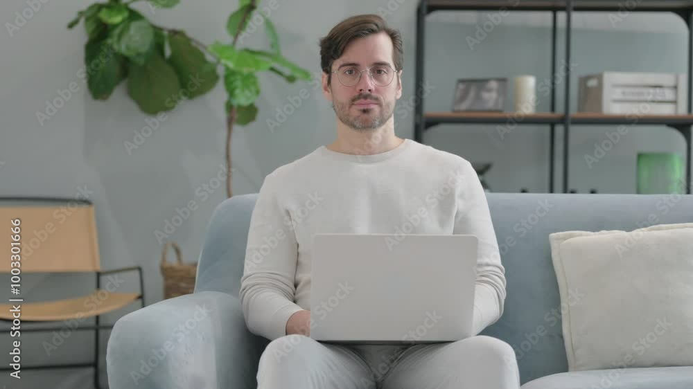 Young Man Looking at Camera while Using Laptop Sitting on Sofa Young Man Looking at Camera while Using Laptop Sitting on Sofa