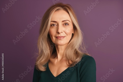 Mature woman with stylish casual attire poses on bright green background. Middle-aged female model wears fashionable dress, has elegant make-up. Confident lady with pretty smile, attractive features.