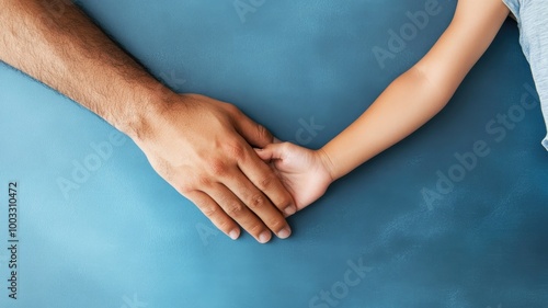 Close-up of adult holding child?s hand on blue surface