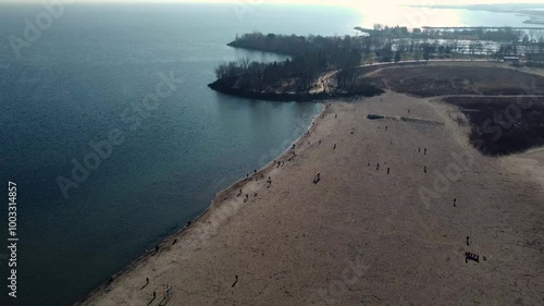 Aerial push-in drone shot of drone flying over the shore of Lake Ontario right by Woodbine Beach. Aircraft is moving forward approaching a group of people that are walking across the waterfront.