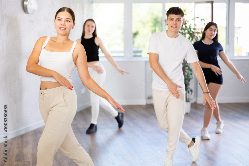 Fototapeta premium Positive female teenager dances vogue in choreographic school, group of young people in sportswear trains together with their classmates in gym before competitions, battle