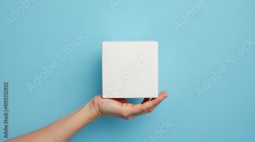 Minimalism concept image with a person hand holding a minimalist plain white cube shape object isolate on an empty blue background